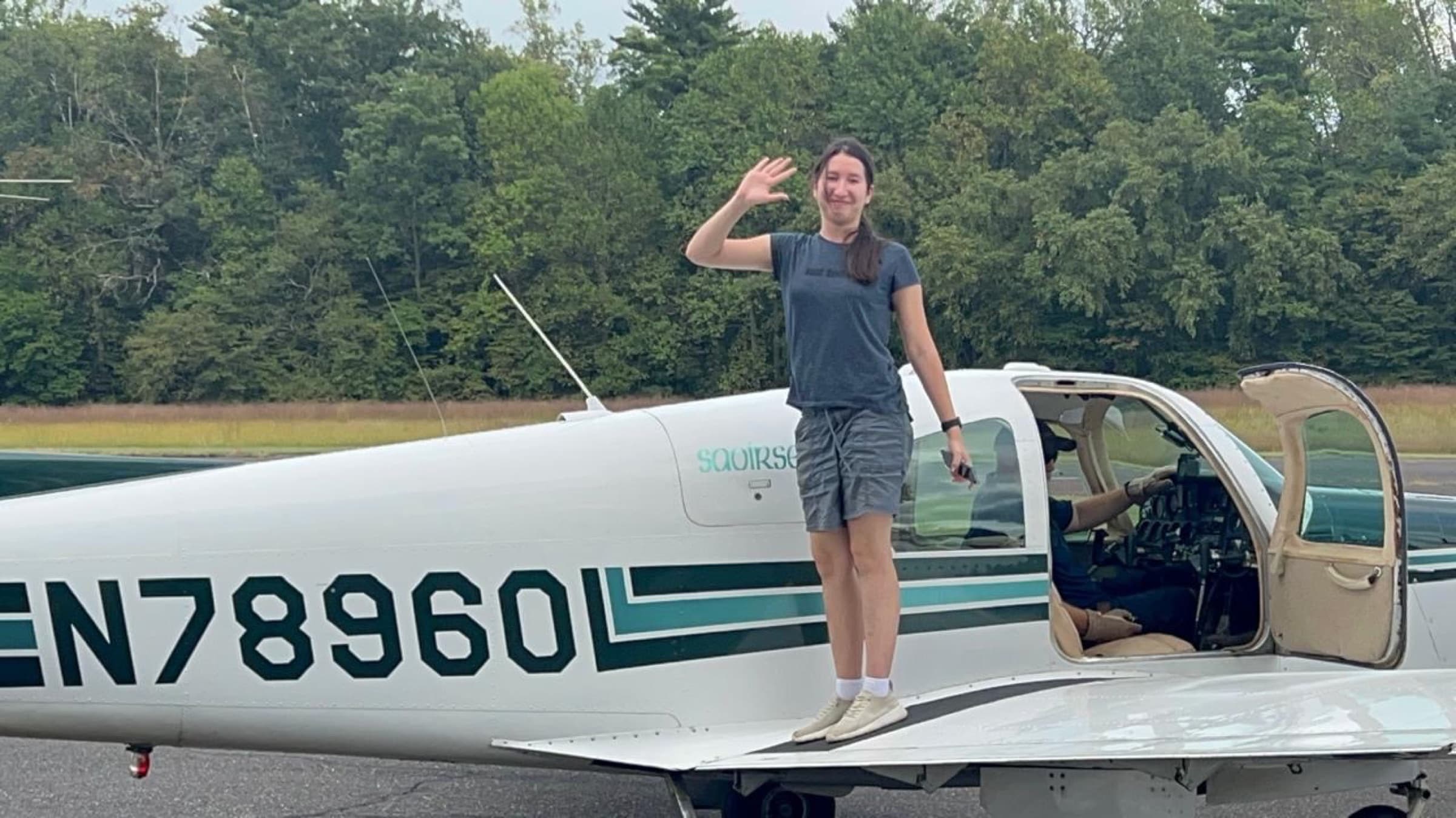 Asel standing on the wing of a small aircraft, waving